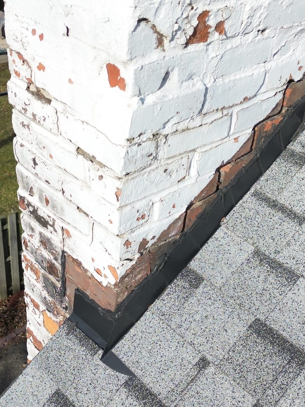 Drone photo of a painted brick chimney and the flashing where it meets the shingles; the drone shadow is visible on the roof